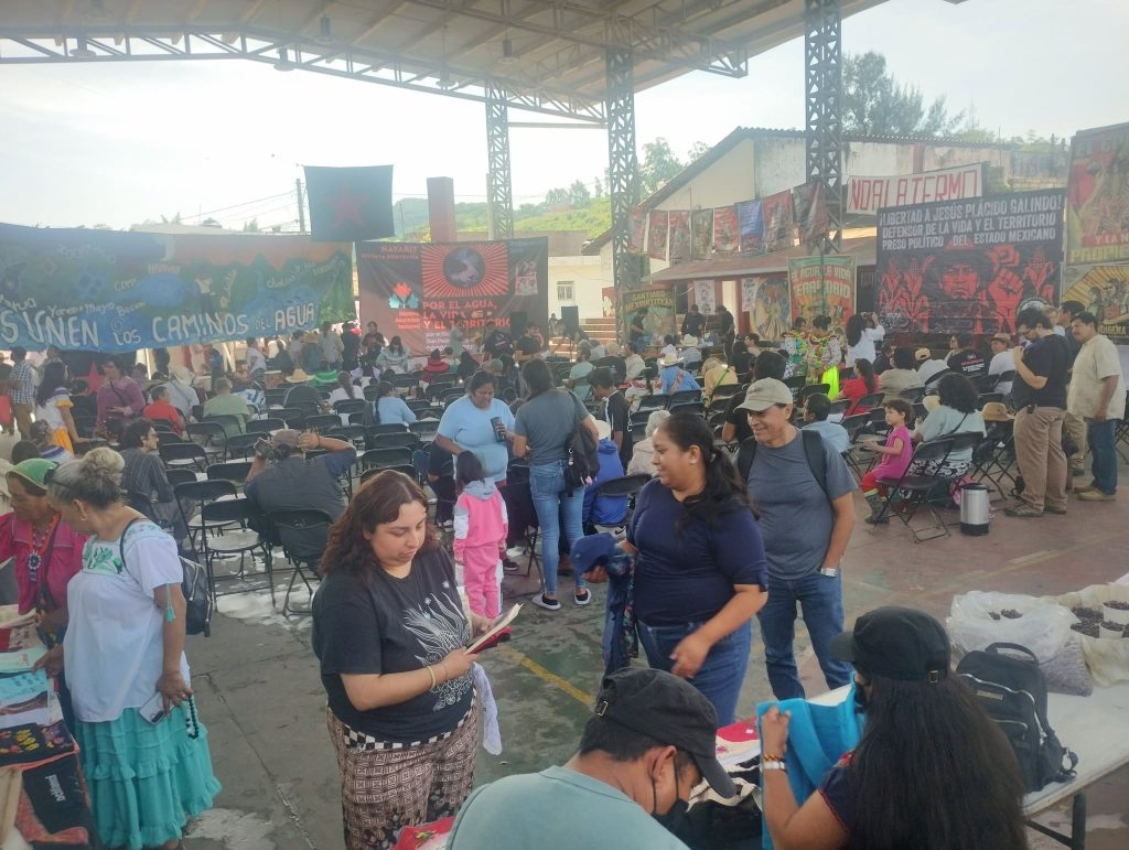 Vista general de la Séptima Asamblea Nacional por el Agua, la Vida y el Territorio en México. Bajo una gran estructura cubierta, numerosas personas de distintas edades participan en el encuentro, rodeadas de pancartas, mantas y carteles de colectivos y comunidades en defensa del agua, los territorios y los derechos de los pueblos.